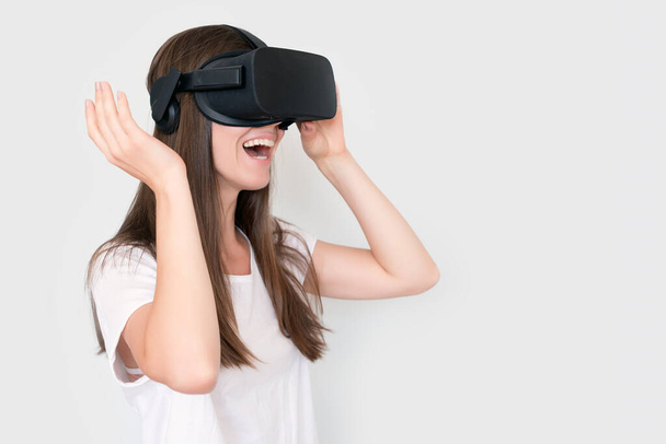 Mladá žena s brýlemi ve virtuální realitě, vr box. Spojení, technologie, nová generace, koncepce pokroku. Dívka se snaží dotknout objektů ve virtuální realitě. Studio záběr na šedou. - Fotografie, Obrázek