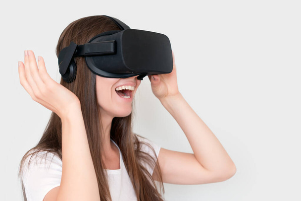Lachende positieve vrouw draagt virtual reality bril headset, vr doos. Verbinding, technologie, nieuwe generatie, vooruitgangsconcept. Meisje probeert objecten aan te raken in virtual reality. Studio shot op grijs. - Foto, afbeelding