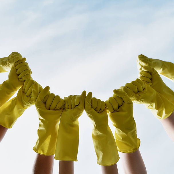 Volunteering. Group of eco activists wearing yellow protective rubber gloves raising hands against blue sky - Photo, image