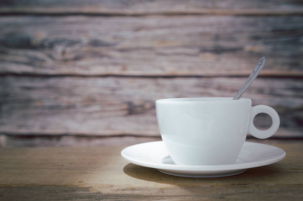 Una tazza di caffè bianco con un cucchiaio nella tazza e un piattino è posto su un piatto di legno e su uno sfondo di legno. - Foto, immagini
