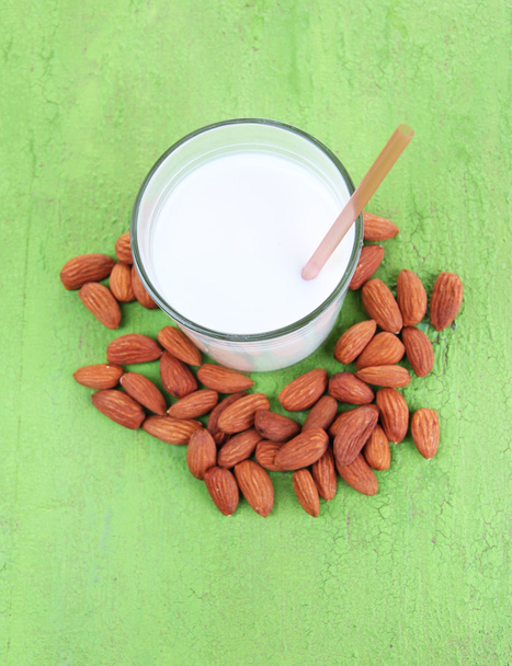 Almond milk in jug with almonds in bowl, on color wooden background - Foto, Imagen