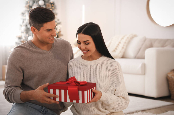 Couple holding gift box in room with Christmas tree - Valokuva, kuva