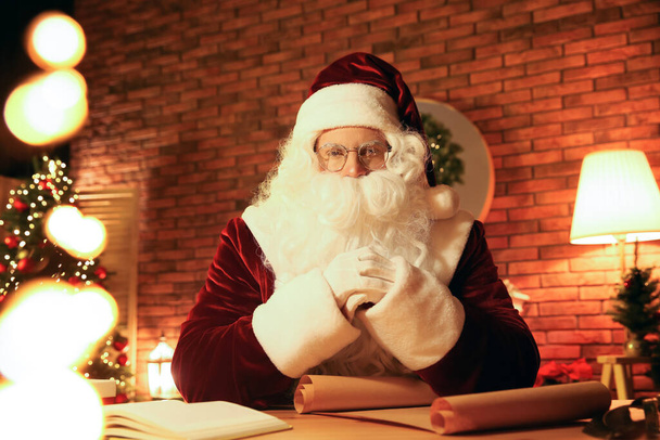 Santa Claus with wish list at table indoors - Фото, зображення
