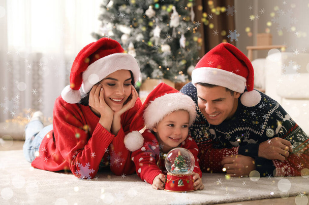Family in Santa hats playing with snow globe at home - Φωτογραφία, εικόνα
