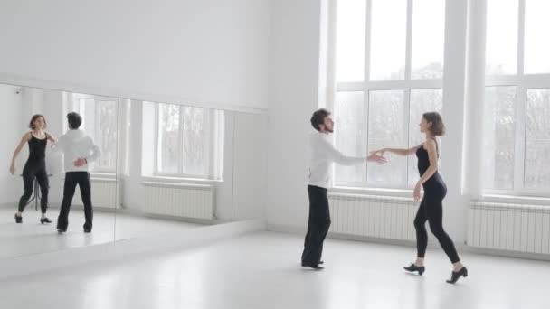Young beautiful couple studying ballroom dance. A professional ballroom dancing couple dances in a large, bright, white hall - Footage, Video