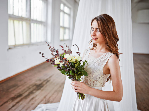 Braut mit Blumenstrauß in einem weißen Zelt in einem Loft-Studio - Foto, Bild