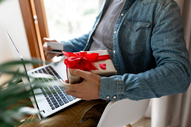 Man using laptop computer and credit card, ordering gifts for Valentines day, Womans Day, Christmas. Shopping online during holidays - Photo, Image