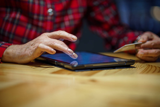 Mature woman makes online purchases using tablet computer in cafe. Older female pays for online payment with credit card. Modern senior uses plastic cards for online shopping. Banking online. - Foto, Imagen