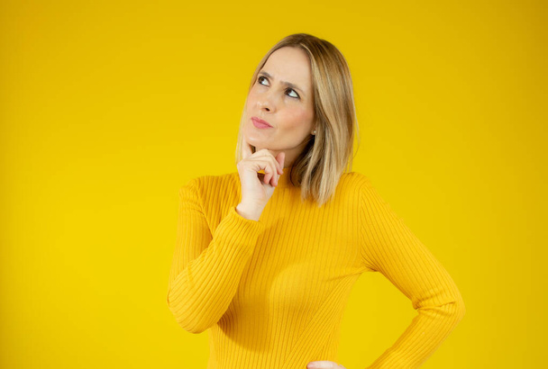 Молодая женщина в обычном свитере с сомнительным жестом на жёлтом фоне. - Фото, изображение