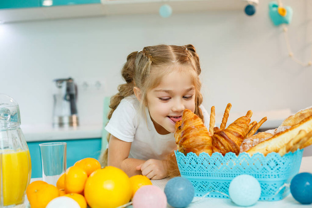 Mała dziewczynka je śniadanie w kuchni z rogalikami i sokiem pomarańczowym.. - Zdjęcie, obraz
