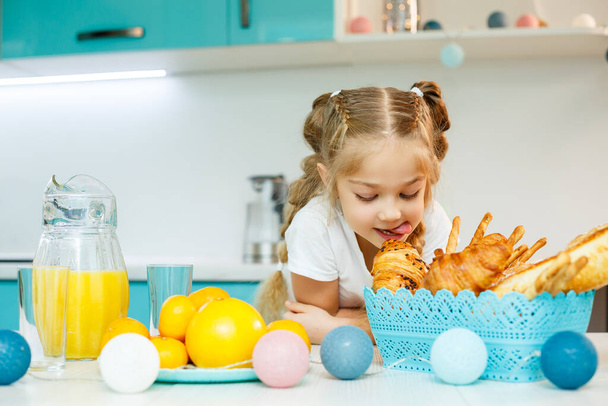 Ένα κοριτσάκι τρώει πρωινό στην κουζίνα με κρουασάν και χυμό πορτοκάλι.. - Φωτογραφία, εικόνα