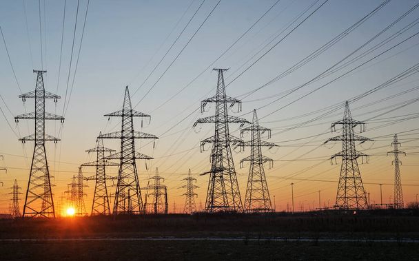 Силуэты высоковольтной электрической башни на фоне восходящего солнца и неба. Селективный фокус - Фото, изображение