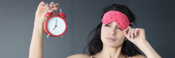 Woman takes off her sleep mask and looks at alarm clock - Foto, Imagen