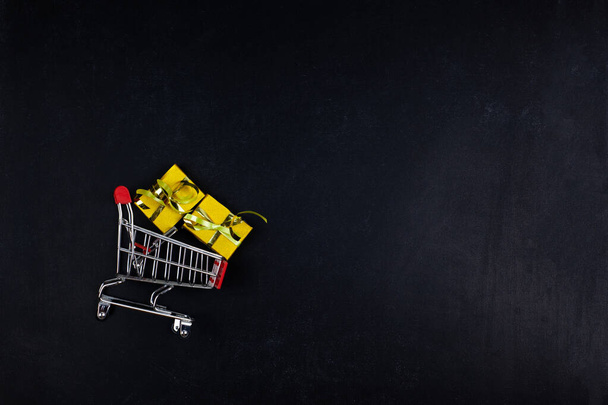 gifts in a shopping trolley on a black background. flat lay. Christmas and black friday sale concept - Zdjęcie, obraz