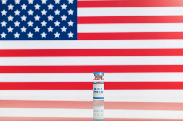 A bottle of vaccine with against American flag - Фото, зображення