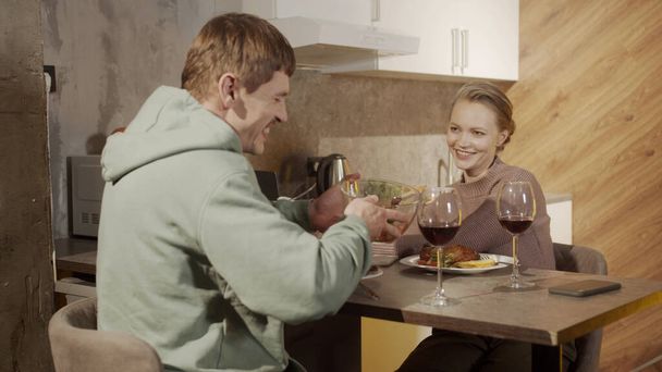 Οι σύζυγοι στο τραπέζι στην κουζίνα διασκεδάζουν μιλώντας και πίνοντας κόκκινο κρασί από ποτήρια. Εορταστικό δείπνο σε ένα αξέχαστο ραντεβού. - Φωτογραφία, εικόνα