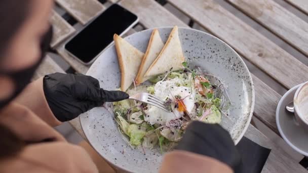 First person view of woman in black gloves hold cutlery. Cafe concept during qurantine. Food outdoors in protective gloves. Fresh vegan salad with shrimps - Footage, Video