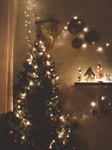 Árvore de Natal em luzes festivas com bugigangas vermelhas e douradas no quarto escuro decorado moderno, véspera de Natal. Preparando casa para férias de inverno. Boas festas e Feliz Natal! - Foto, Imagem