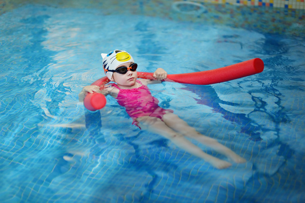 klein meisje leren om te zwemmen met zwembad noodle - Foto, afbeelding