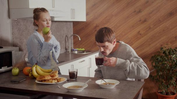 Dívka připravila večeři pro svého muže. Ten chlap jí polévku a pije kafe. Dívka jí zelené jablko a mluví. - Fotografie, Obrázek