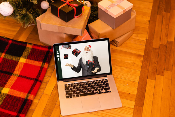 Chat-Anruf mit dem Weihnachtsmann auf einem Laptop in einem geschmückten Raum zu Weihnachten. Weihnachtsmann online. - Foto, Bild