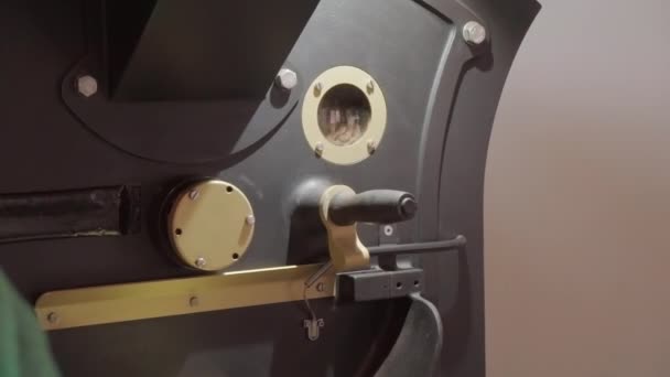 Van dichtbij bekeken beelden van onherkenbare fabrieksarbeider die de roostermachine bestuurt met koffiebonen die van binnen roteren - Video
