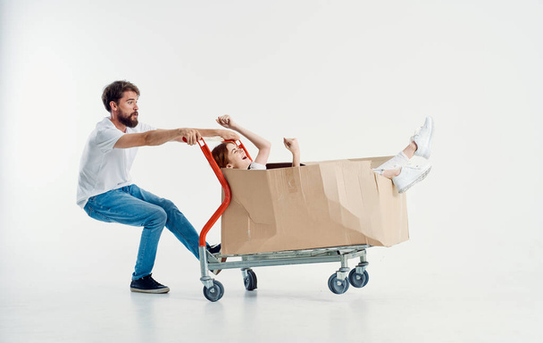 γυναίκα σε ένα κουτί σε ένα τρόλεϊ φορτίου και ένα χαρούμενο αρσενικό courier σε ένα ελαφρύ φόντο - Φωτογραφία, εικόνα