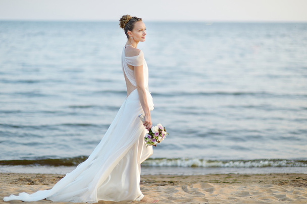 Bride walking along sea coast on sunset - Фото, зображення