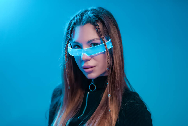 Cool cyberpunk portrait of a young woman. Woman in futuristic neon glasses. - Фото, изображение