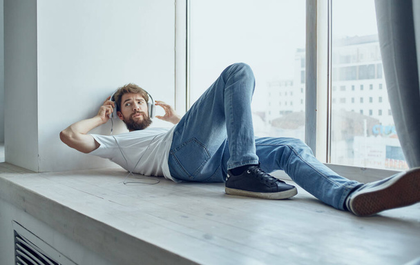 bearded man lying on the windowsill wearing headphones music - Fotografie, Obrázek