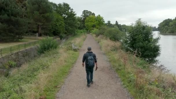 4k Luftaufnahme eines Mannes, der auf einem Wanderweg neben einem Fluss wandelt, während er seine Mütze wechselt - Filmmaterial, Video