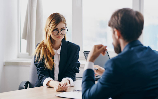 Un hombre de negocios con traje y una mujer se comunican en el trabajo uno frente al otro en la mesa de la oficina - Foto, Imagen