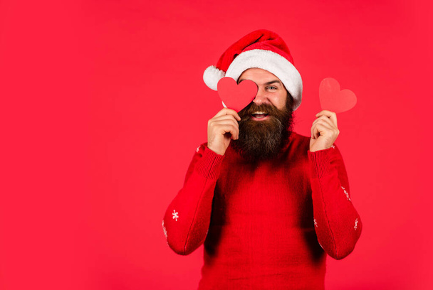 Szerelembe esni. Én is szeretlek. Hideg napok. Meleg szívek. Üdvözöllek a szívedben. Jóképű férfi szereti téli ünnepek piros háttér. Télapó sapkát visel. Boldog karácsonyt és boldog új évet! - Fotó, kép