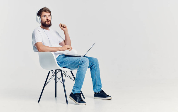 mężczyzna w słuchawkach z laptopem na kolanach siedzi na krześle komunikacji izolowane tło - Zdjęcie, obraz