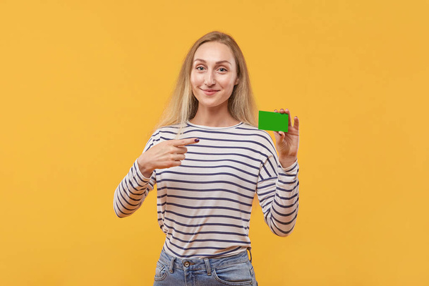 A young beautiful blonde woman points to an empty green card. - Fotografie, Obrázek