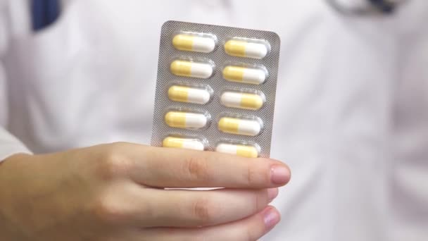 Pillole antidolorifiche nella mano femminile di un medico con un cappotto bianco. Capsule con medicinali, assunzione di farmaci, assistenza sanitaria, farmacia e concetto di trattamento, vista da vicino - Filmati, video