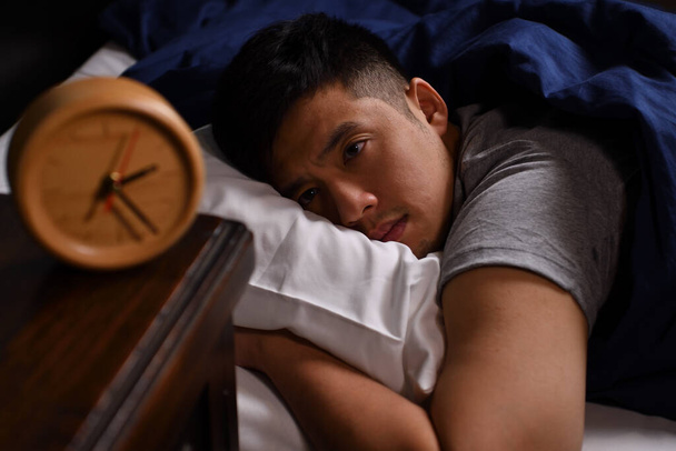 Депресивний молодий чоловік, який страждає від безсоння лежить у ліжку
 - Фото, зображення
