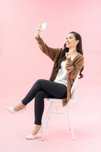 Улыбающаяся молодая женщина делает селфи фото на смартфоне на розовом фоне - Фото, изображение
