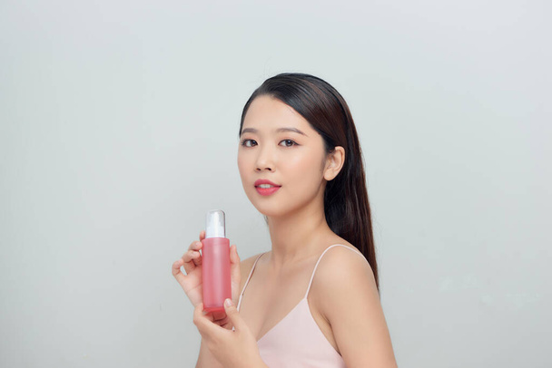 Jonge vrij stijlvolle vrouw over witte muur achtergrond holding fles met cosmetica water. - Foto, afbeelding