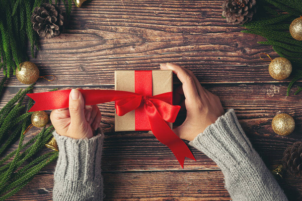 mano de mujer sosteniendo una caja de regalo con cinta roja en el suelo de madera - Foto, Imagen