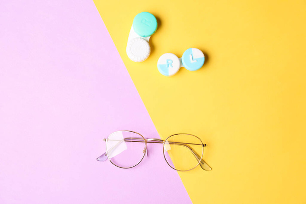 Containers with contact lenses and eyeglasses on color background - Fotó, kép