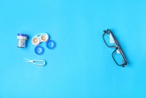 Контейнер с контактными линзами, пинцетом и очками на цветном фоне - Фото, изображение