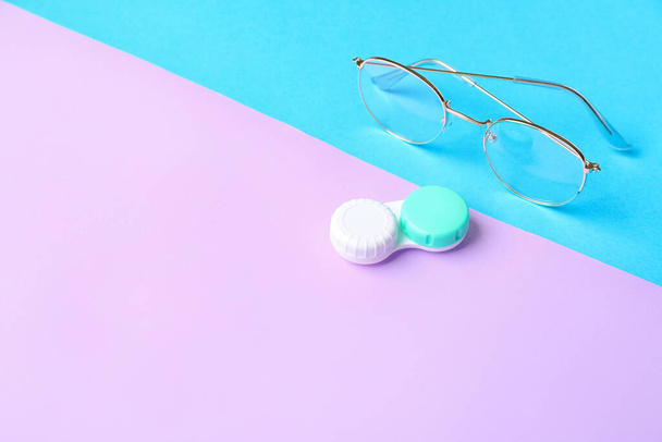 Container with contact lenses and eyeglasses on color background - Foto, Imagem