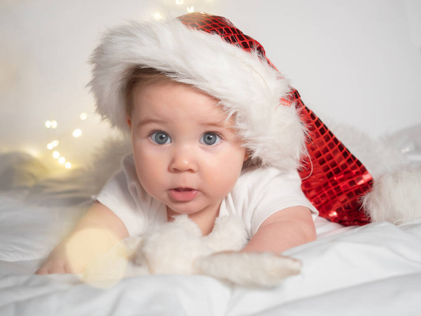 Adorable baby girl in Santa hat lying on the bed - 写真・画像