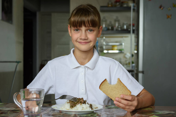 Portret van een gelukkig meisje dat dineert aan tafel in de keuken - Foto, afbeelding