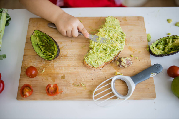 Vrouwelijke handen verspreiden avocado op een sneetje brood boven snijplank - Foto, afbeelding