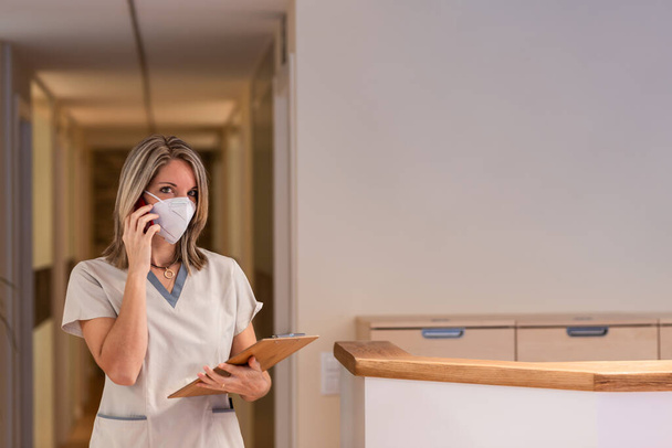 infermiera risponde al telefono con una cartella e una maschera protettiva in ospedale - Foto, immagini