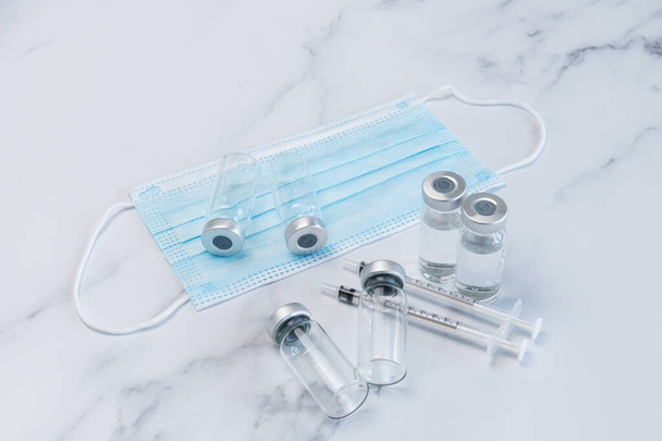 Quatre ampoules vaccinales et deux seringues sur un comptoir en marbre le long de deux ampoules médicales vides. Un masque facial EPI est également inclus dans le - Photo, image
