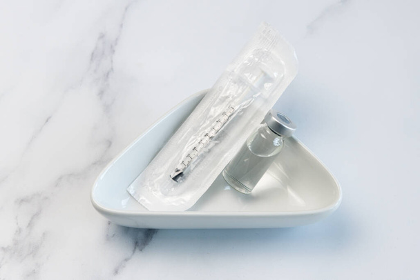 One Vaccine Ampule and One Syringe in Plastic Packaging lying loosely in a Medical ceramic container. - Foto, Imagen