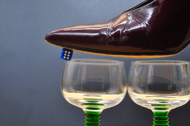 σύνθεση με θηλυκό παπούτσι ισορροπημένη σε ζάρια στηρίζεται σε γυαλιά. Εννοιολογική φωτογραφία για τους κινδύνους του τζόγου. - Φωτογραφία, εικόνα